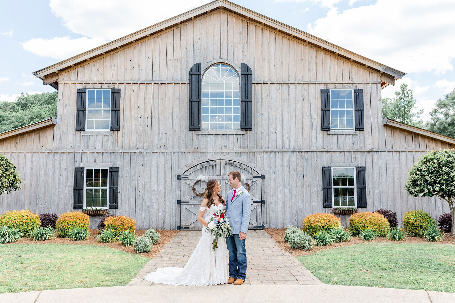 married couple looking at each other standing in front of barn